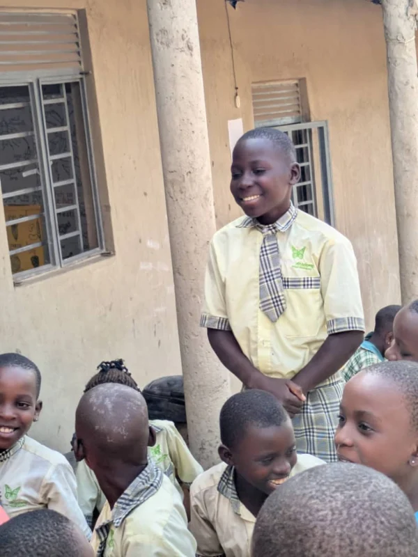 A pupil in Ubuntu Academy uniform standing to speak while classmates sit and listen