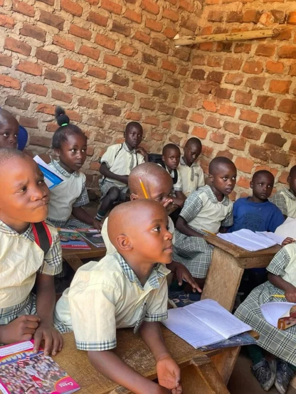 A full classroom of pupils at wooden desks in a brick-walled room, looking towards the teacher