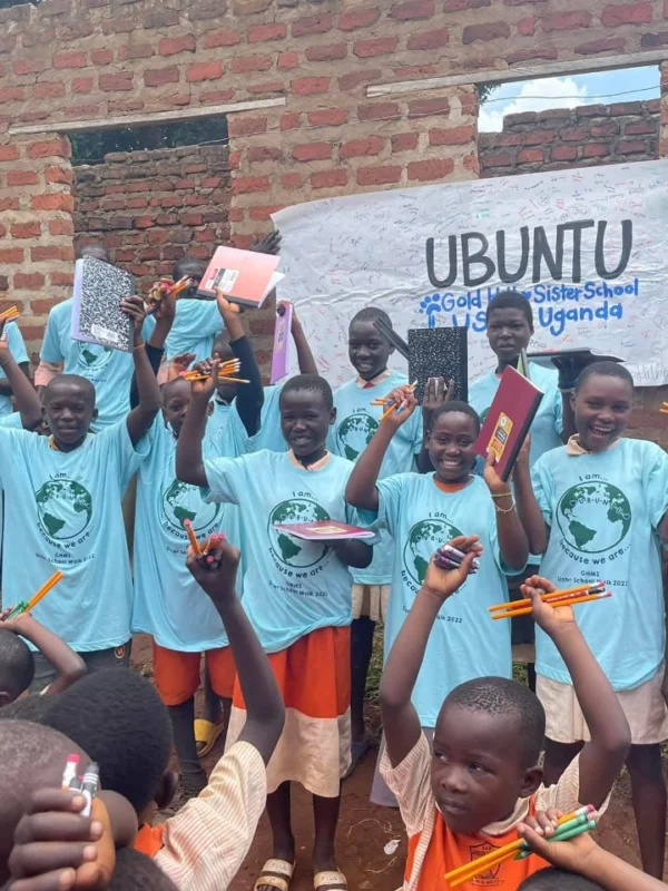 Pupils in Gold Hill Sister School T-shirts holding up new pencils and exercise books under a signed Ubuntu banner